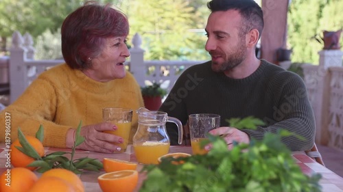 Mother and son having breakfast with freshly squeezed orange juice surrounded by oranges in a country house surrounded by nature