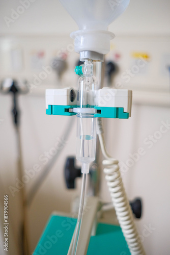 A close-up of a medical intravenous (IV) drip chamber and tubing set against a blurred clinical background.