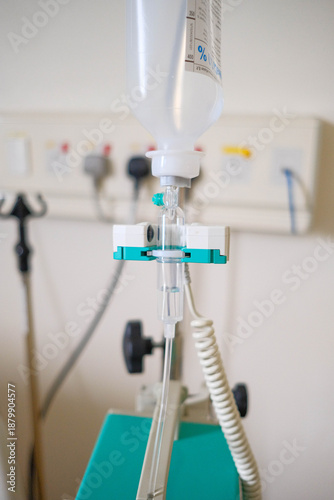 A close-up of a medical intravenous (IV) drip chamber and tubing set against a blurred clinical background.