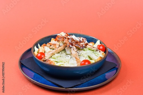 Chicken Caesar salad with grilled chicken, crispy bacon, croutons and cherry tomatoes isolated on orange background