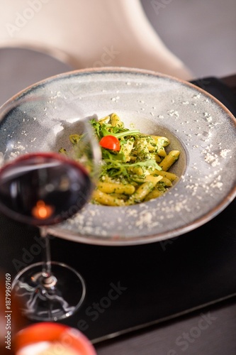 Pasta with green pesto sauce served in elegant bowl with red wine glass in fine dining restaurant atmosphere