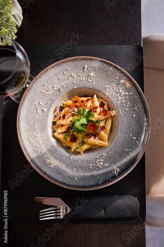 Top view of creamy pasta with crispy bacon and arugula served in elegant bowl at fine dining restaurant table