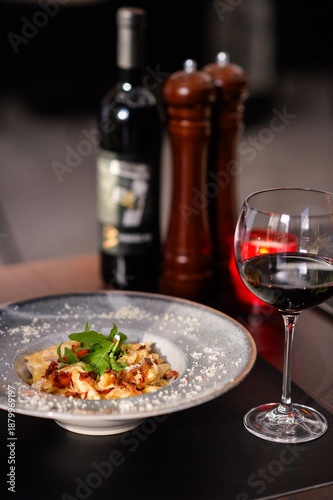 Gourmet creamy pasta with crispy bacon and arugula served with red wine in elegant fine dining restaurant setting