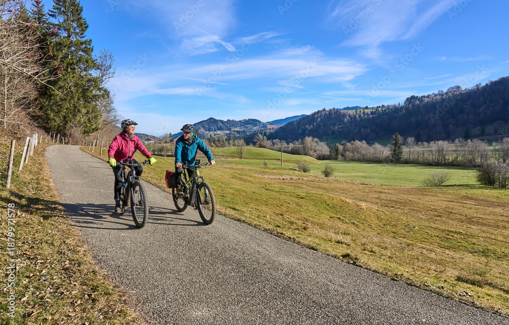 Naklejka premium elderly couple rides electric mountain bikes on a trail in the Allgäu Alps near Oberstaufen in Bavaria. The scene depicts a wintry mountain landscape in early winter.