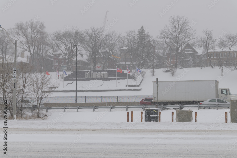 Fototapeta premium City of Toronto sign on the side of a hill facing Gardiner Expressway, public transit rails, and Lake Shore Blvd W, during a major weather event on 2026-01-15