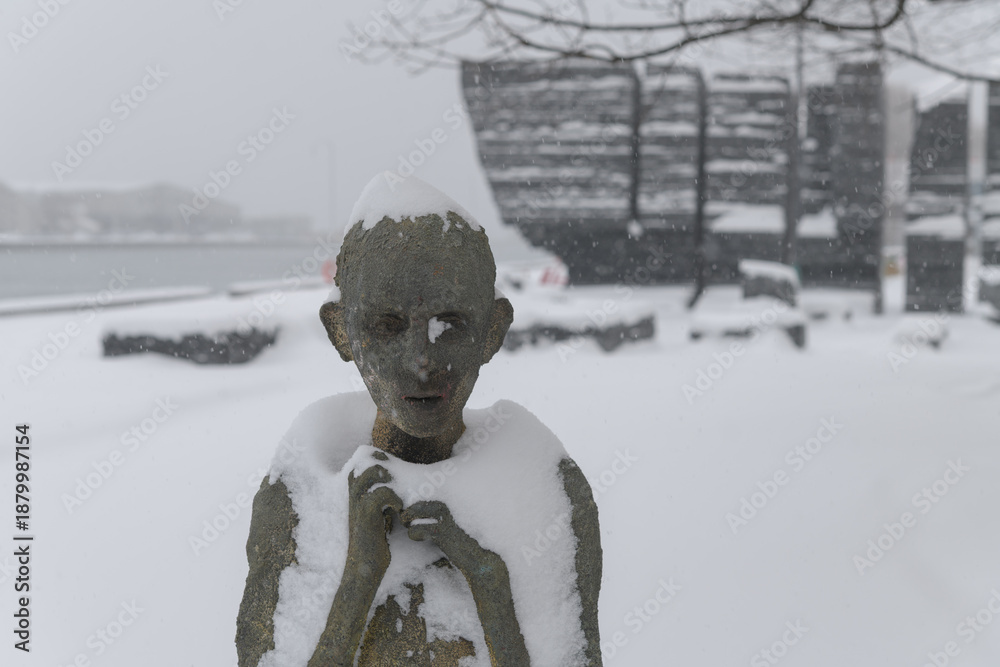 Fototapeta premium front of Child Emigrant created by Irish artist Rowan Gillespie part of The Arrival, set beside the old Canada Malting silos on Eireann Quay, Toronto, during winter storm on 2026-01-15