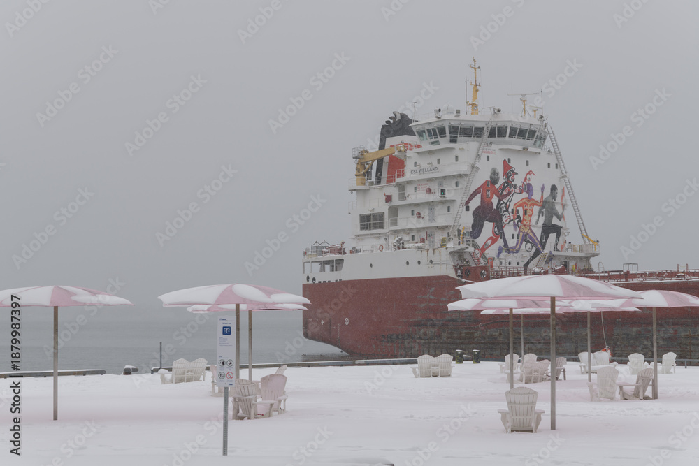 Fototapeta premium CSL Welland (self-unloading bulk carrier) with sugar cargo docked at Redpath Sugar Refinery located at, 95 Queens Quay E, during a snow storm on 2026-01-15 in Toronto (Sugar Beach view)