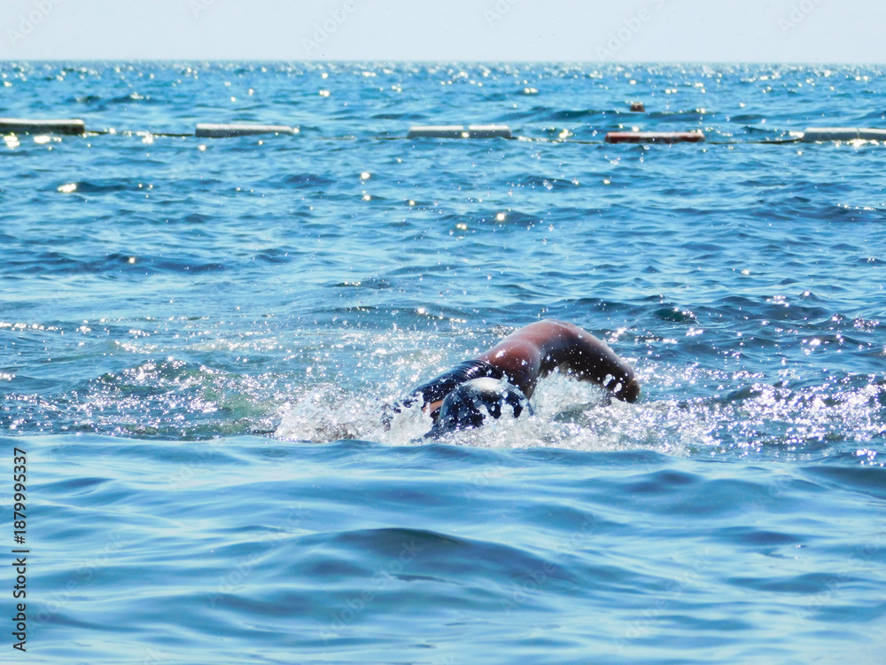 Fototapeta premium A scene on the seashore, a young person with a swimming scarf and sports shirt photographed while swimming