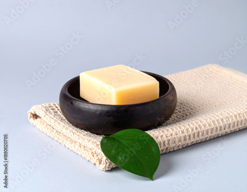 Natural soap bar on folded towel with green leaves, minimalist spa concept