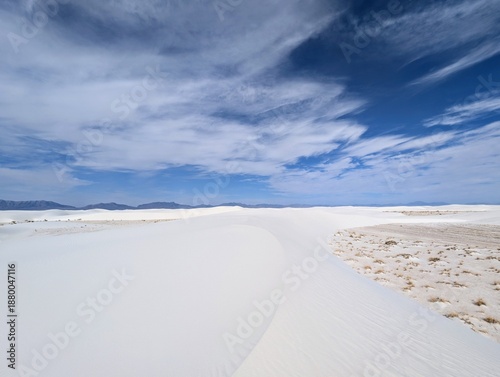 A serene and expansive desert landscape unfolds with pristine white sand dunes stretching into the distance under a brilliant blue sky dotted with wispy clouds