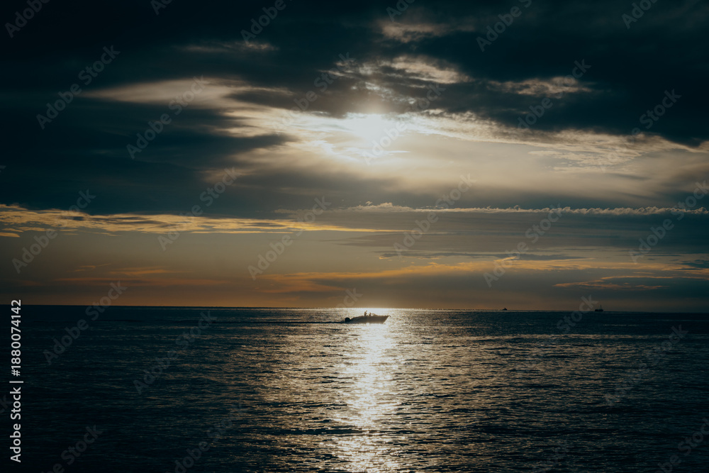 Obraz premium Stimmungsvolle Abendstimmung an der Küste von Istrien in Kroatien: Ein Motorboot fährt über das Meer vor dem Horizont, während die Sonne untergeht, Istrien, Kroatien