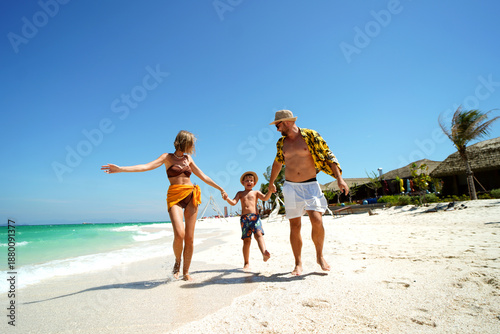 Happy family with a child holding hands and having fun on a beautiful tropical beach. Summer vacation, travel and lifestyle concept. 