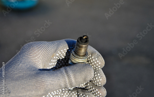 Close-up of a gloved hand holding an old spark plug covered in black carbon soot. Engine malfunction diagnostics, fuel mixture problems, car maintenance service.