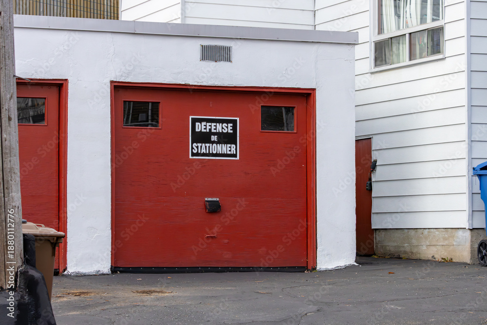 Naklejka premium Canada, Quebec, 08 November 2025 : Red garage doors with French no parking sign above entrance area