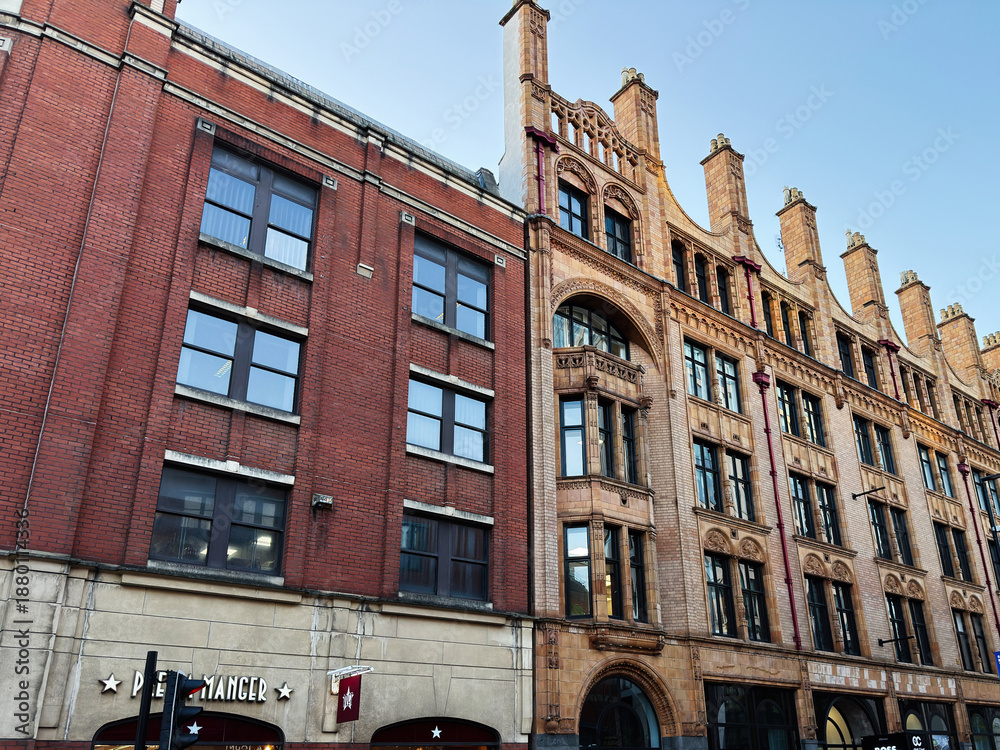 Fototapeta premium Historic brick and stone building along Manchester street with shops and pedestrians in the UK