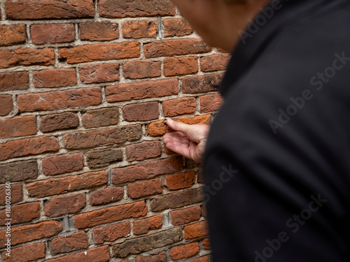 Fotografía Close-up of hand touching weathered red-orange brick wall showing aging and wear