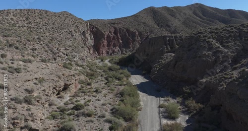 Drone aerial through narrow Tabernas Desert canyon in Almeria Spain, steep rocky walls and dry wash below, cinematic arid gorge landscape with dramatic textures and depth