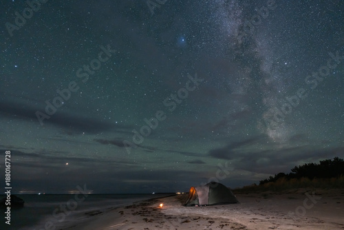 Tent with a warm light on a sandy beach under a spectacular Milky Way starry sky in wild Estonian nature.