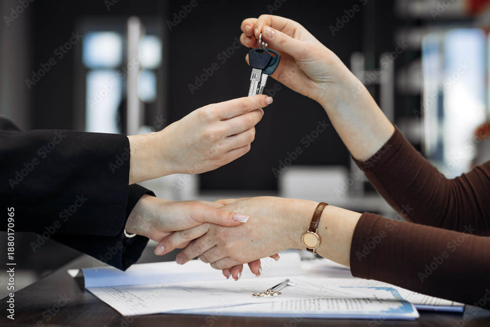 Obraz premium Hands exchanging car keys in a modern office setting with documents and a desk visible, representing a vehicle purchase or rental transaction in a professional environment