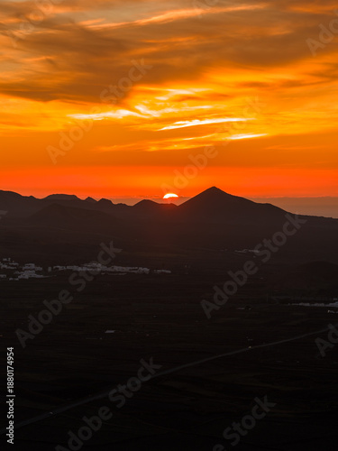 Photography Fiery orange and gold clouds streak the sky as the sun sets over Lanzarote