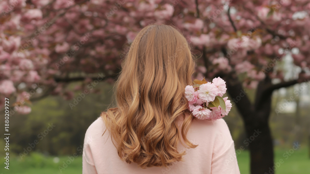 Naklejka premium woman with long hair and flowers in a park with blooming trees
