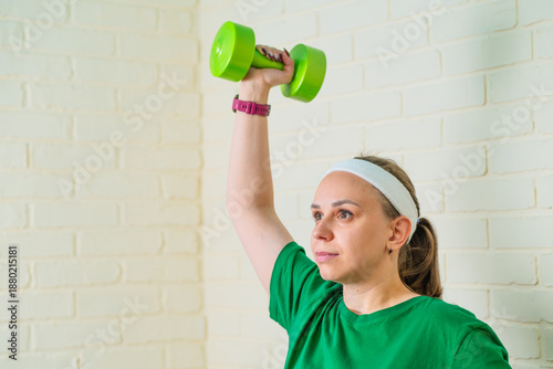 Quadro su tela A woman exercises with a bright green dumbbell in a home gym, focusing on streng