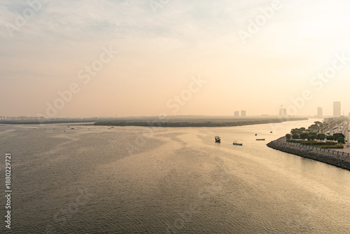 Ras Al Khaimah, UAE, 12.10.2025. Sunset over Mangrove Forest with boats and city skyline in the background on a hazy evening.