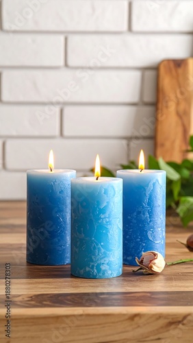 Three lit blue candles stand on a wooden surface against a brick wall and greenery background