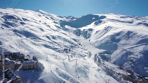 Aerial 4K video from a drone to Sierra Nevada ski resort on a sunny winter day in the mountains, Spain. Sierra Nevada is the largest mountain range near the city of Granada in Spain with snow. Sierra 