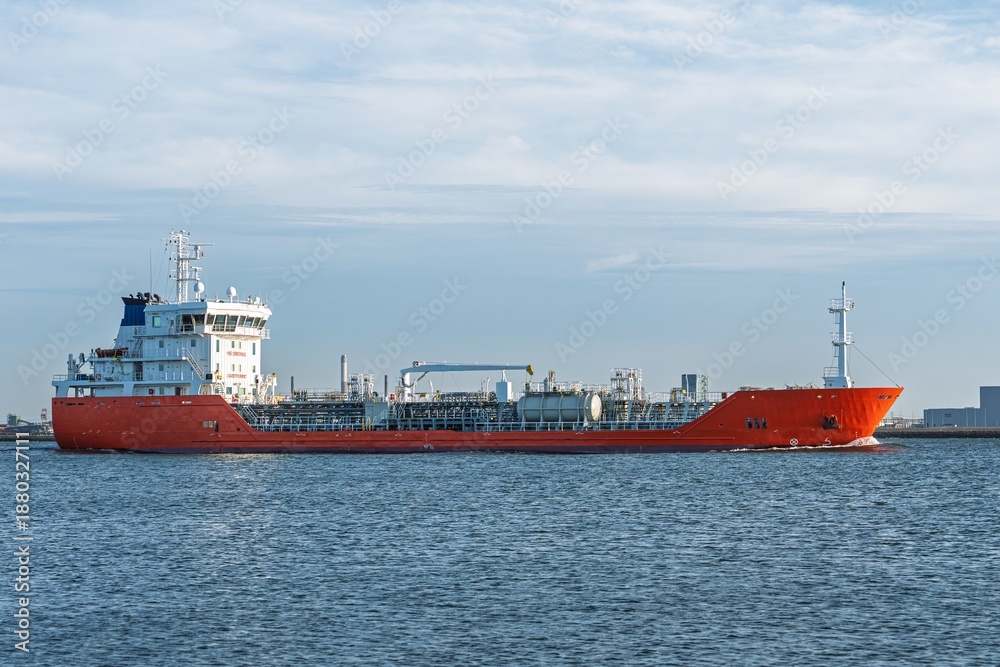 Fototapeta premium A striking photograph of an orange tanker navigating calm waters under a sky filled with soft clouds. Ideal for maritime themes or promotional use, showcasing the beauty of maritime industry.