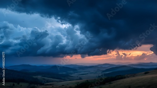 Dramatic stormy landscape with dark clouds and orange sunset over rolling hills and mountains