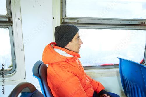 Fotografie Man in orange jacket sitting on empty local train looking thoughtfully outside