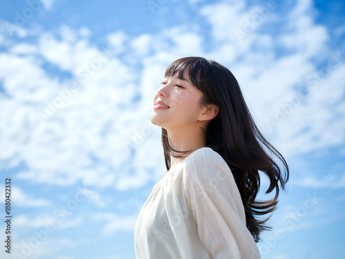 青空と長い髪が風になびく日本人女性 Generative AI