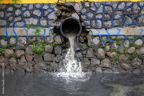Foto Liquid waste sewage flowing from concrete pipe on stone river wall into dark grey murky water canal with stone texture