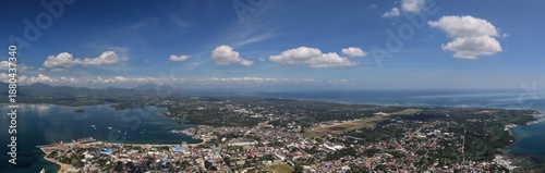 Expansive panoramic aerial photograph of Puerto Princesa City showcasing urban development, airport, coastal waters, and mountain backdrop in Palawan, Philippines.