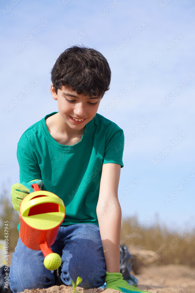 Naklejka premium smiling child, planting a small plant and watering it with a watering can
