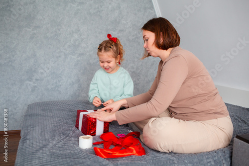 Side view of adult mother and her daughter pack a gift together for Valentine's Day and Mother's Day. Caucasian woman and a cute little girl spend time together