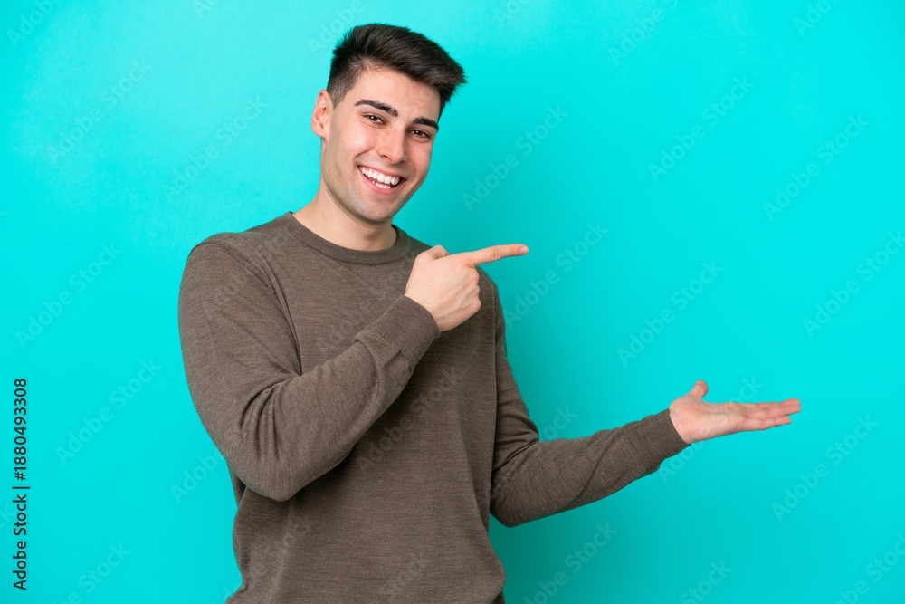 Fototapeta premium Young caucasian man isolated on blue background holding copyspace imaginary on the palm to insert an ad