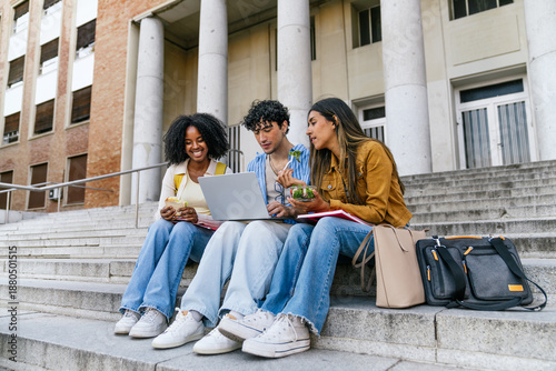 Obraz na płótnie Multiracial university students using a laptop, chatting, and eating on campus s
