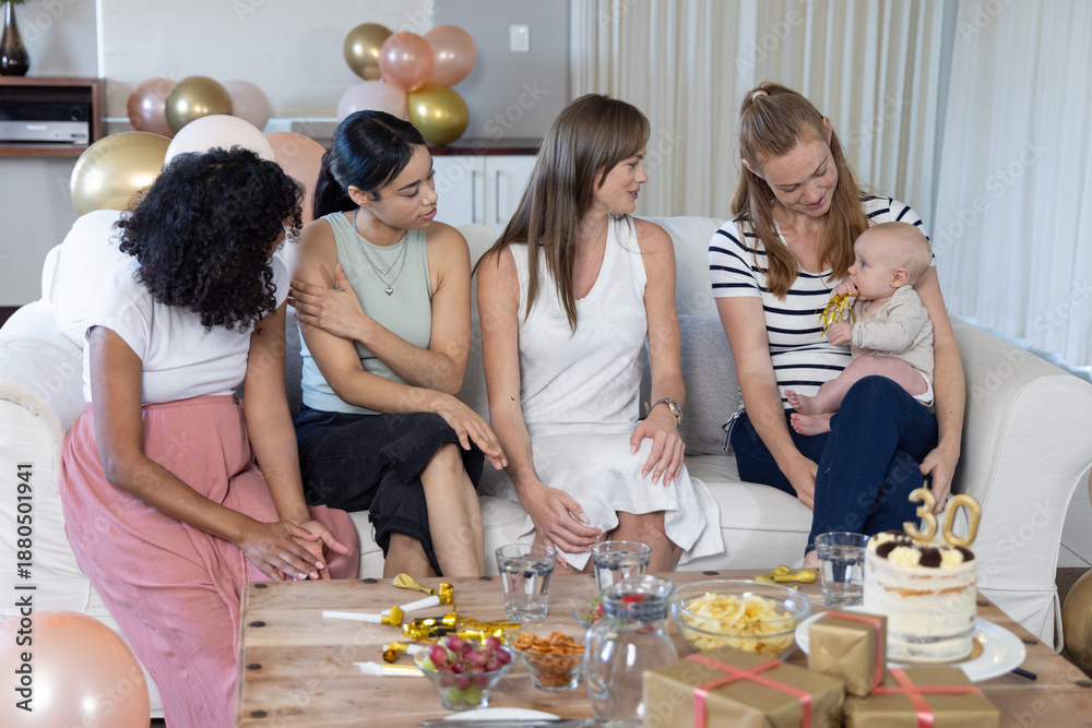 Obraz premium Diverse female friends celebrating turning thirty with baby in living room with cake, balloons