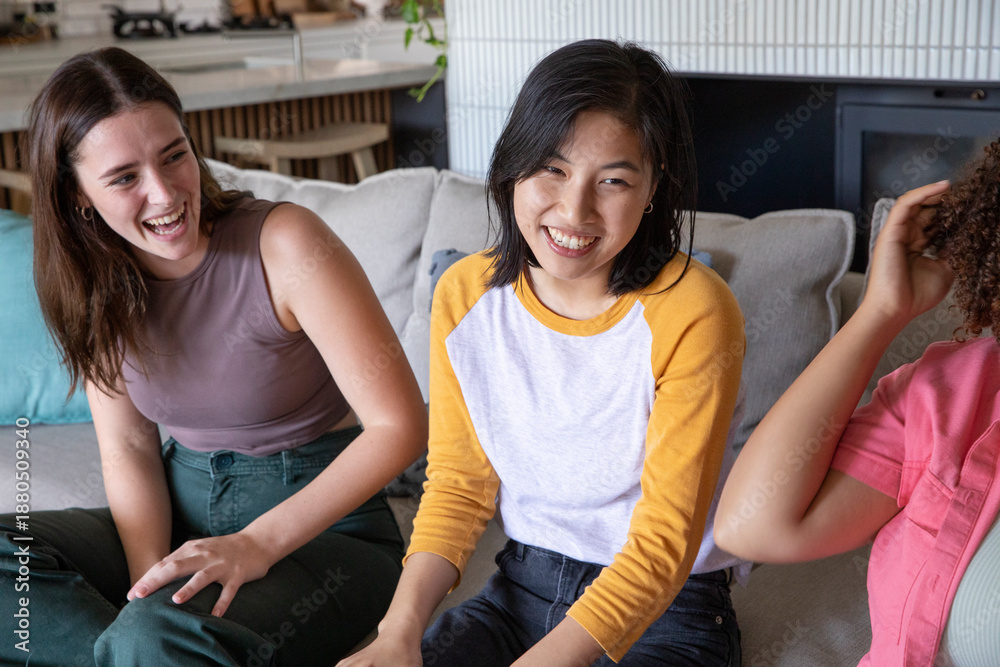 Fototapeta premium Diverse female friends sitting on light sofa in lounge with cushions, bar stools and hanging plant