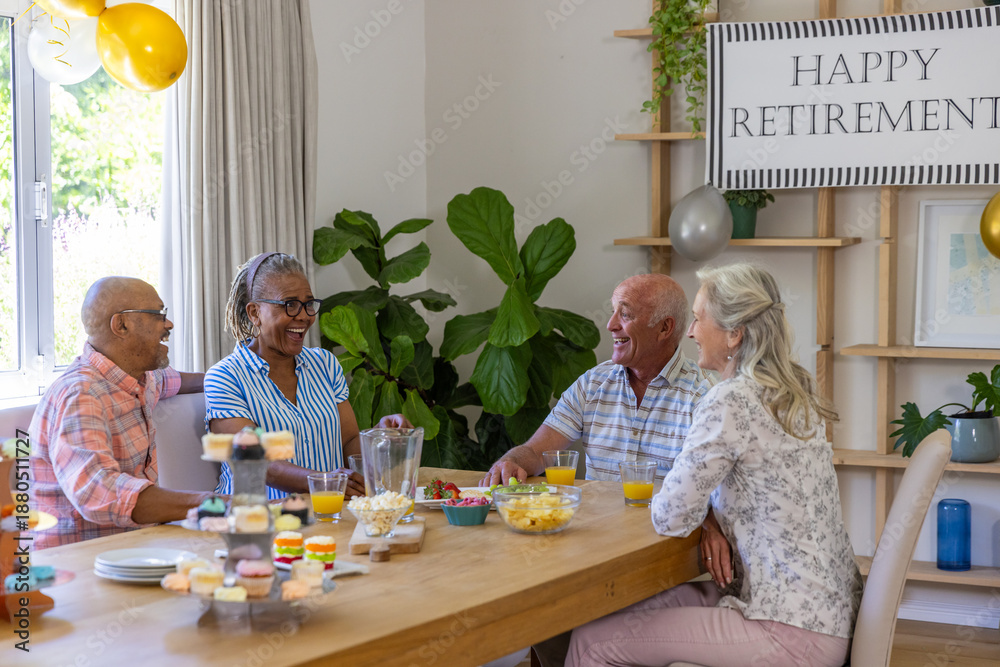 Obraz premium Diverse senior friends celebrating retirement at home dining table with cupcake stand, banner