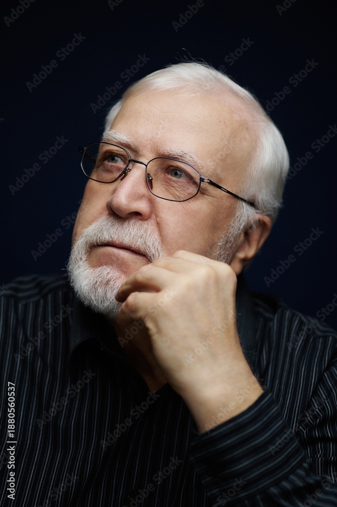 Obraz premium Elderly man with glasses and white beard thinking about life in a dark room