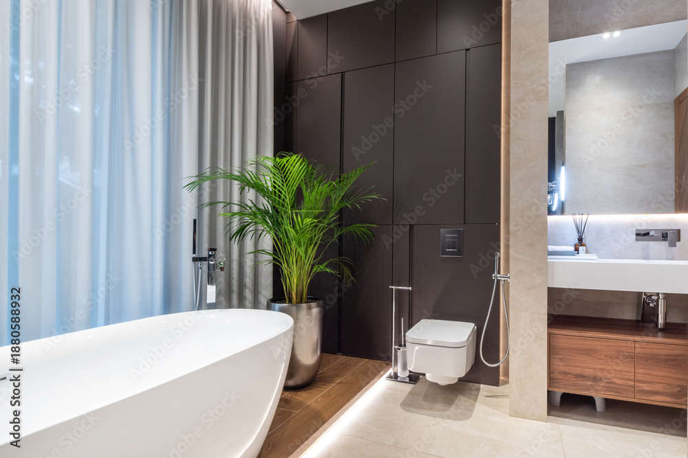 Fototapeta premium Excellent bathroom design with beautiful finishes. A bathtub by the window, a potted palm tree, stylish lighting.