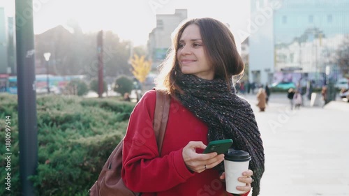 A pretty young woman uses her mobile phone while walking through the streets of a European city on a warm autumn day.