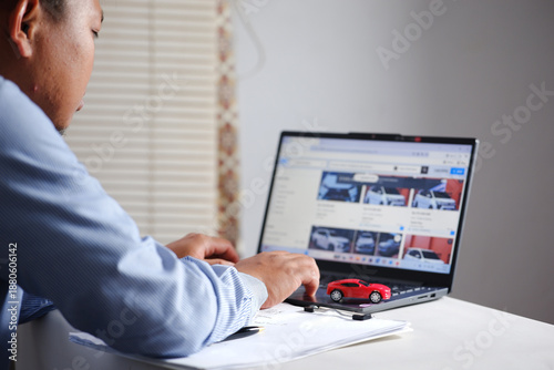 Buying and selling cars online. A man wants to buy a used car. He's browsing through numerous used car listings online on his laptop to compare prices. Many automobiles with picture detail.
