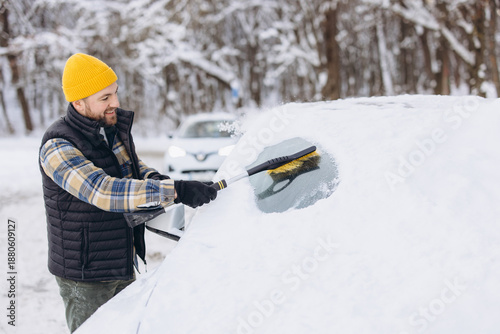 Man scraping snow and ice from car windshield in winter weather, vehicle clearing for safe driving