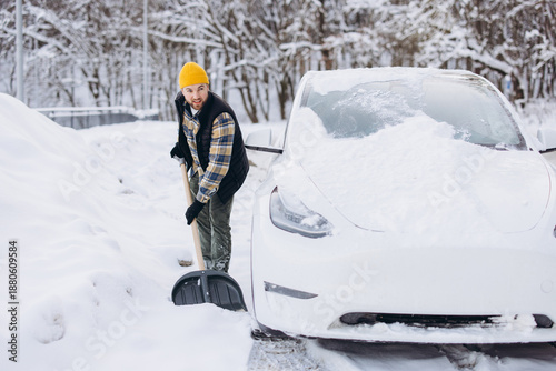 фотографія Man shoveling snow from around an electric vehicle after heavy snowfall during f