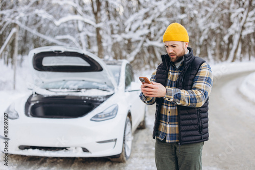Φωτογραφία Frustrated man calling for help with flat electric vehicle battery or breakdown