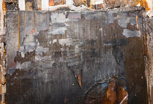 Φωτογραφία Charred wooden walls from a fire disaster peel in layers of soot and flaking gray paint, exposing warped beams in dark